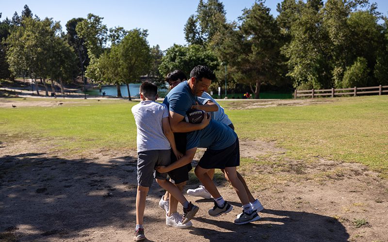 A group of people enjoy a game of touch football in a grassy park area, with trees and a pond in the background—one of the many fun things to do in Simi Valley.