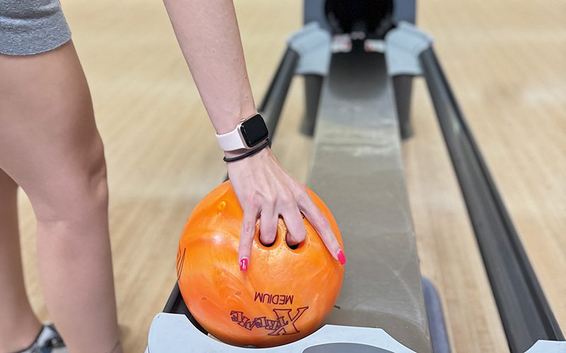 In Simi Valley, where entertainment options abound, a person with a smartwatch and pink nails expertly picks up an orange bowling ball from a return rack.